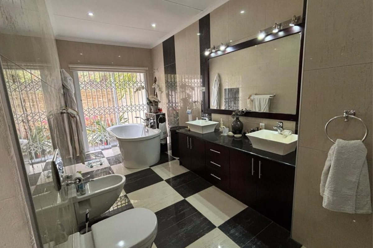 Spacious modern bathroom featuring a double vanity with vessel sinks, a freestanding bathtub, bidet, toilet, and large wall mirror with integrated lighting.