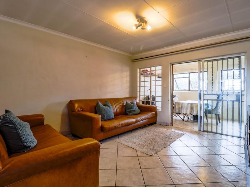 A living room featuring tiled flooring, coved ceilings, and a sliding glass door with a security gate leading to an adjacent space.