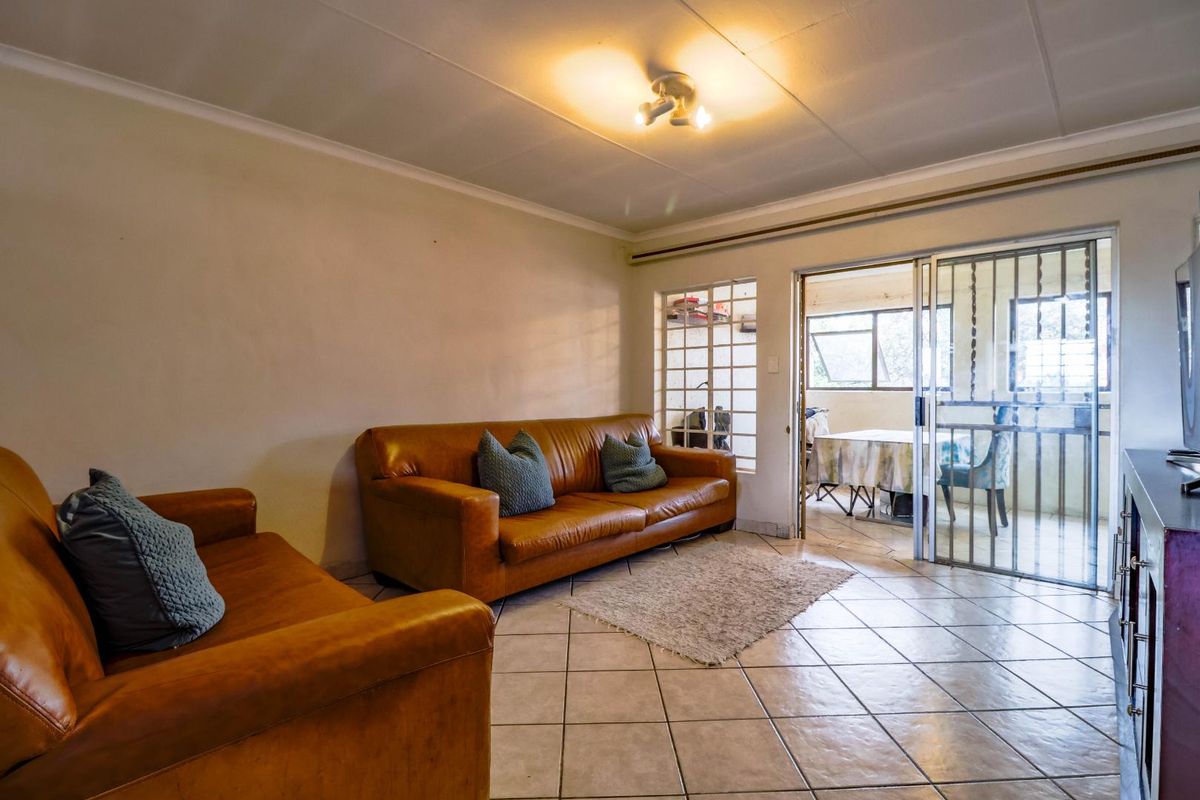 A living room featuring tiled flooring, coved ceilings, and a sliding glass door with a security gate leading to an adjacent space.