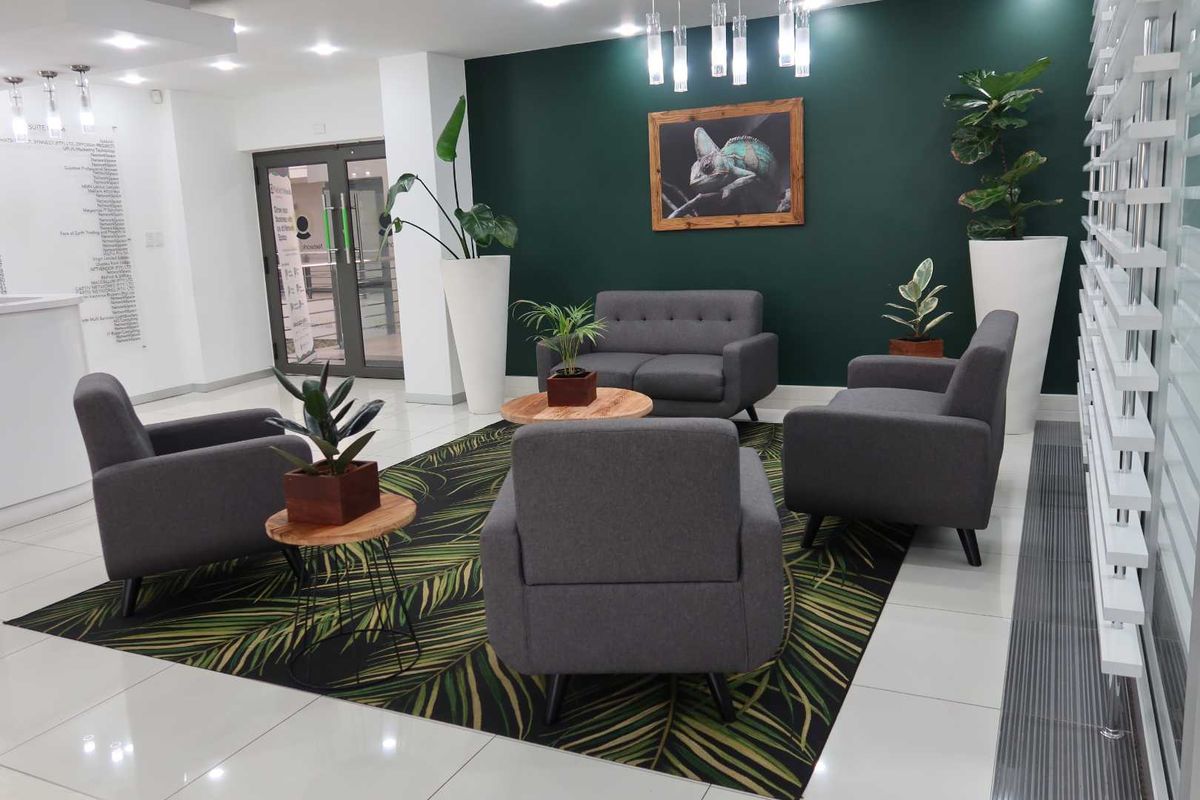 A modern, well-maintained office reception area featuring polished tiled floors, a bold green accent wall, and glass entrance doors.