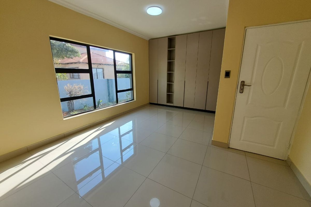 A bright, empty bedroom featuring large windows, polished floor tiles, and built-in floor-to-ceiling cabinetry.