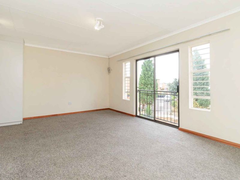 A spacious, empty bedroom featuring neutral walls, carpeted flooring, a built-in wardrobe, and a sliding glass door leading to a small balcony.