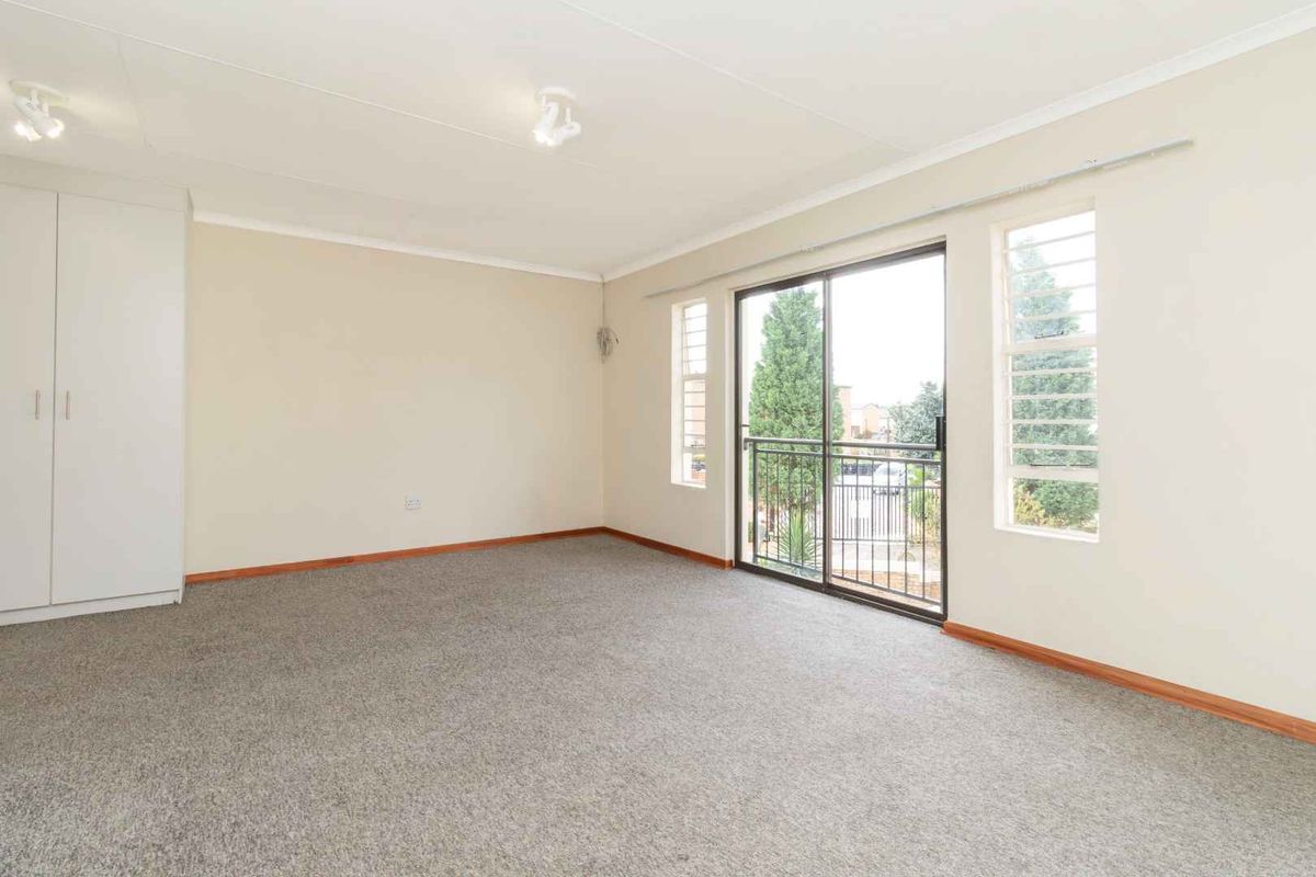 A spacious, empty bedroom featuring neutral walls, carpeted flooring, a built-in wardrobe, and a sliding glass door leading to a small balcony.