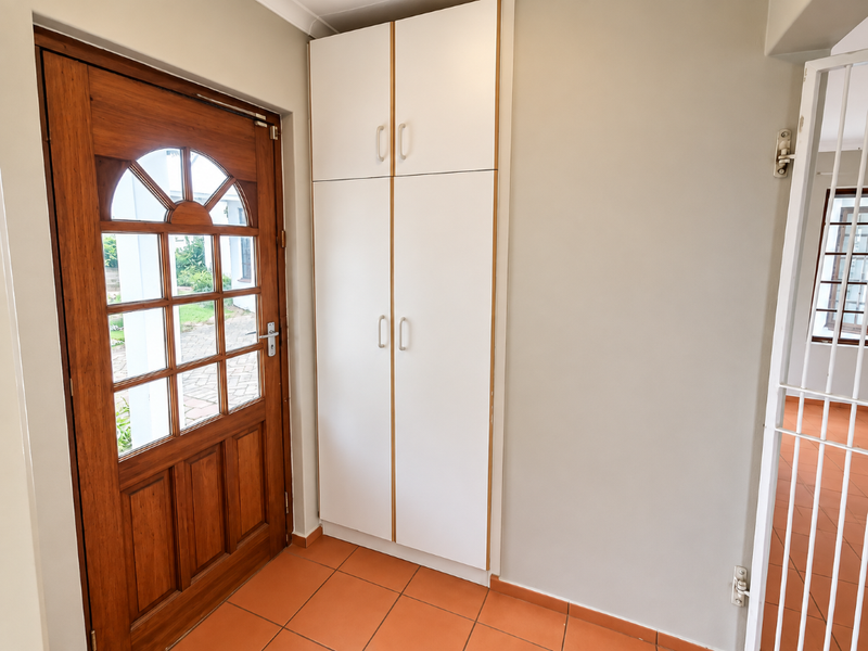 A bright entrance area featuring a classic timber front door, built-in storage cabinetry, and durable terracotta floor tiles.
