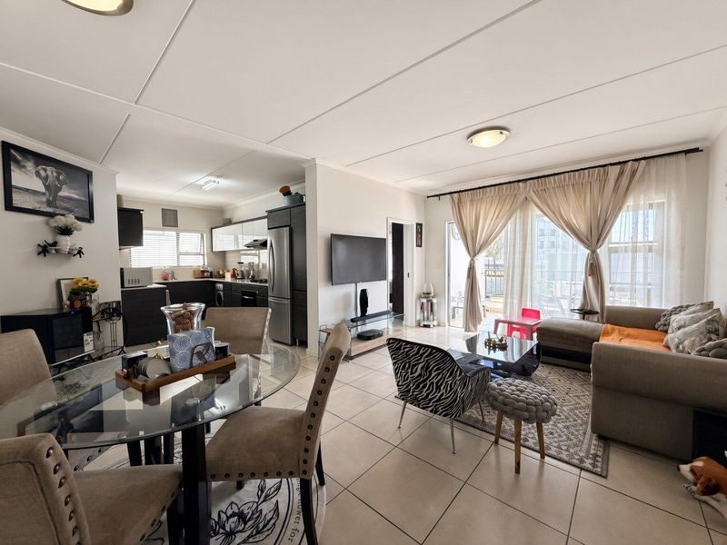 Open-plan living and dining area featuring tiled floors, a modern kitchen with built-in cabinetry, and a sliding glass door leading to an outdoor space.