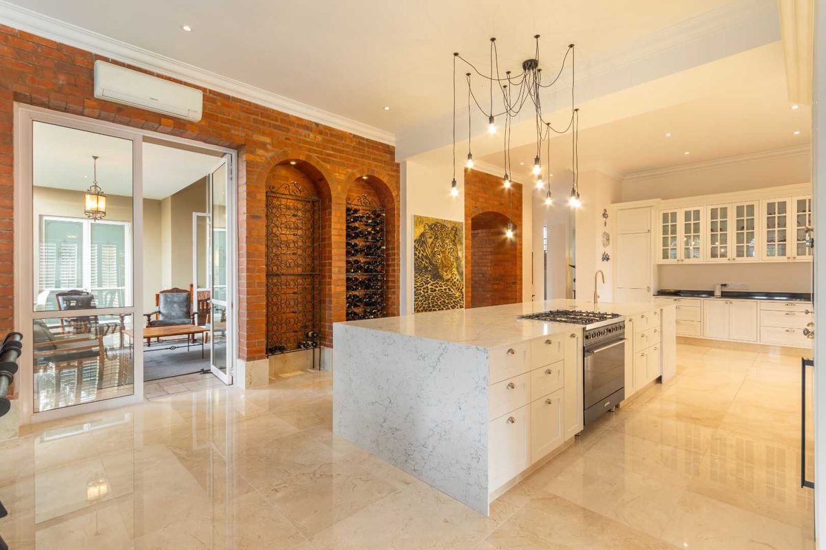 Spacious kitchen featuring a large stone-topped island with integrated gas cooktop, custom cabinetry, exposed brick feature wall, and seamless access to the patio.
