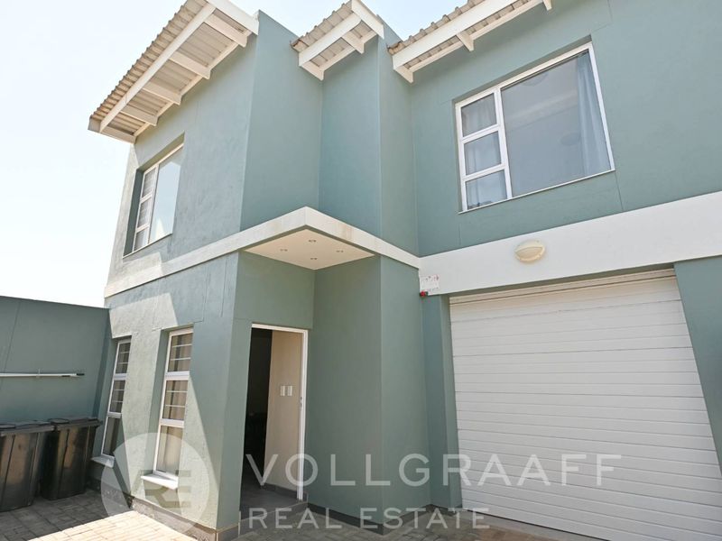 Front elevation of a modern townhouse featuring a single garage, paved driveway, and contemporary exterior paint finish.