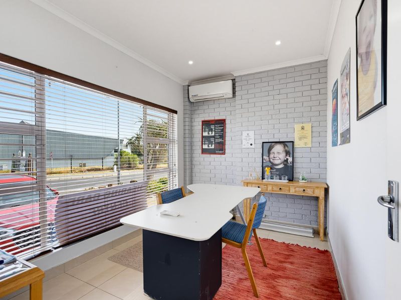 A bright office space featuring a large window with venetian blinds, an exposed brick feature wall, and a wall-mounted split-system air conditioner.