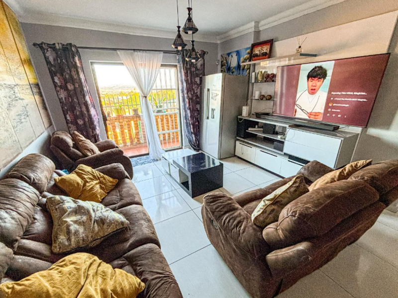 A comfortable living room featuring tiled flooring, a built-in media unit, and a sliding glass door providing access to an outdoor balcony area.