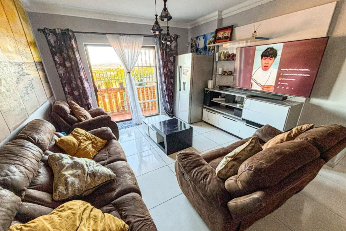 A comfortable living room featuring tiled flooring, a built-in media unit, and a sliding glass door providing access to an outdoor balcony area.