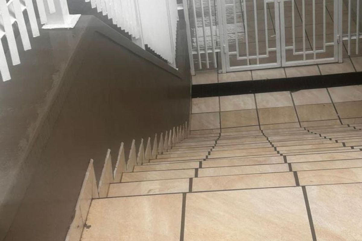 A tiled staircase leading to a secure metal entrance gate with white metal balustrades.