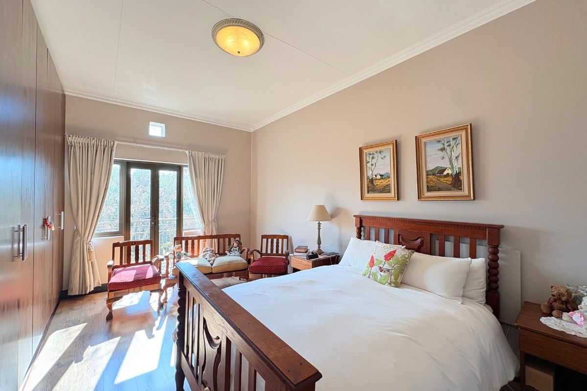 A well-maintained bedroom featuring built-in wooden cupboards, laminate flooring, and double doors leading to a private balcony.