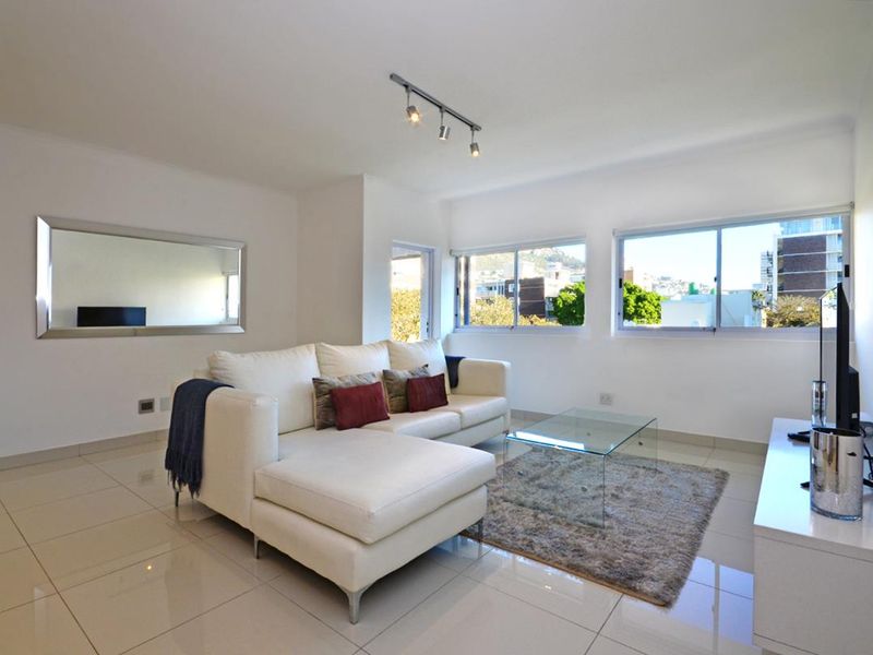 Bright and modern living room featuring polished tiled flooring, track lighting, and large windows providing natural light and urban views.