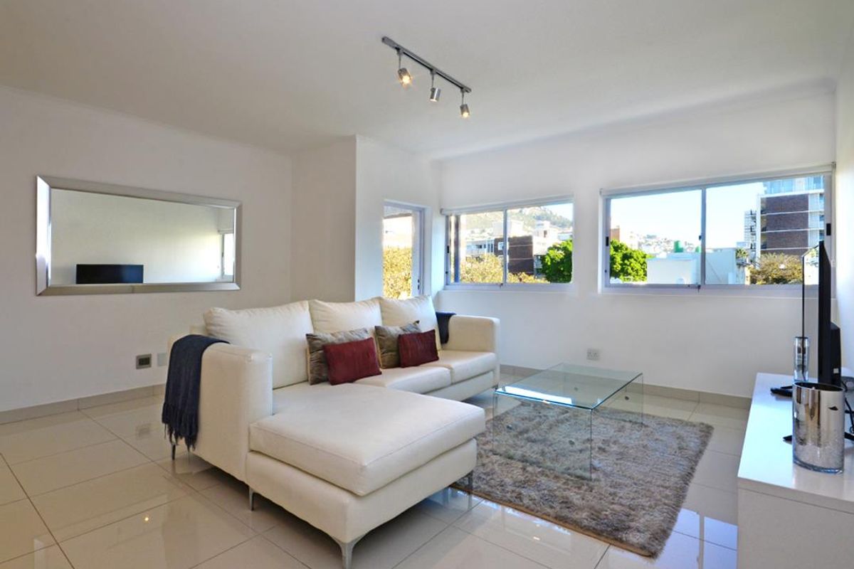 Bright and modern living room featuring polished tiled flooring, track lighting, and large windows providing natural light and urban views.