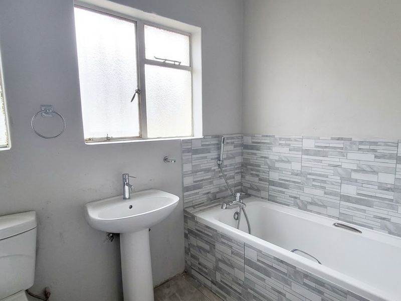 A functional bathroom featuring a pedestal basin, a bathtub with tiled surround, and a toilet, requiring minor cosmetic updates to the walls and flooring.