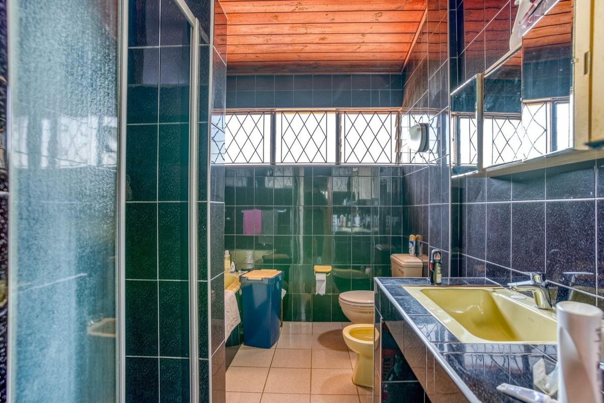 A dated bathroom featuring dark wall tiles, a timber ceiling, a built-in vanity with an integrated sink, and a separate shower enclosure.