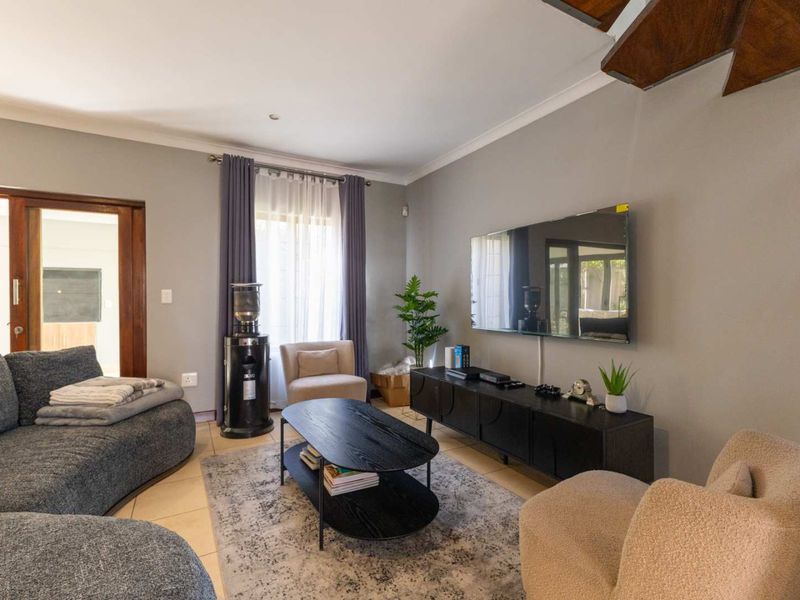 A comfortable living room featuring tiled flooring, recessed downlights, and a wooden staircase, with direct access to an adjacent room through a sliding door.