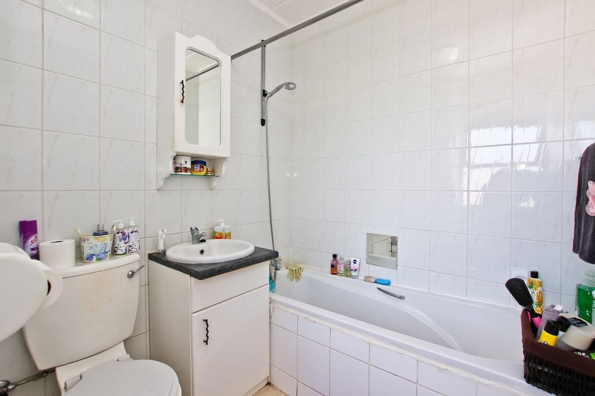 A compact bathroom featuring a white bathtub with shower attachment, a vanity basin, and a toilet, finished with white wall tiling.