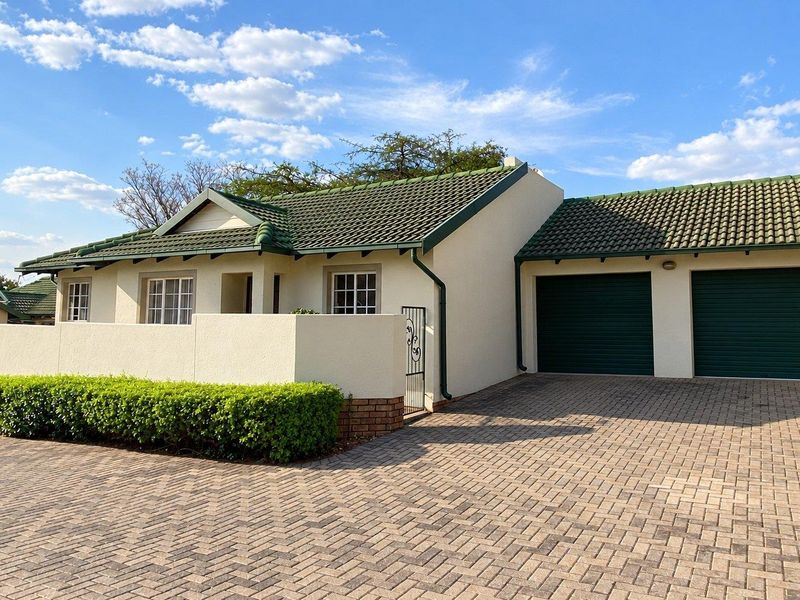 Front view of a townhouse featuring a double garage, paved driveway, and a well-maintained exterior with a tiled roof and boundary wall.