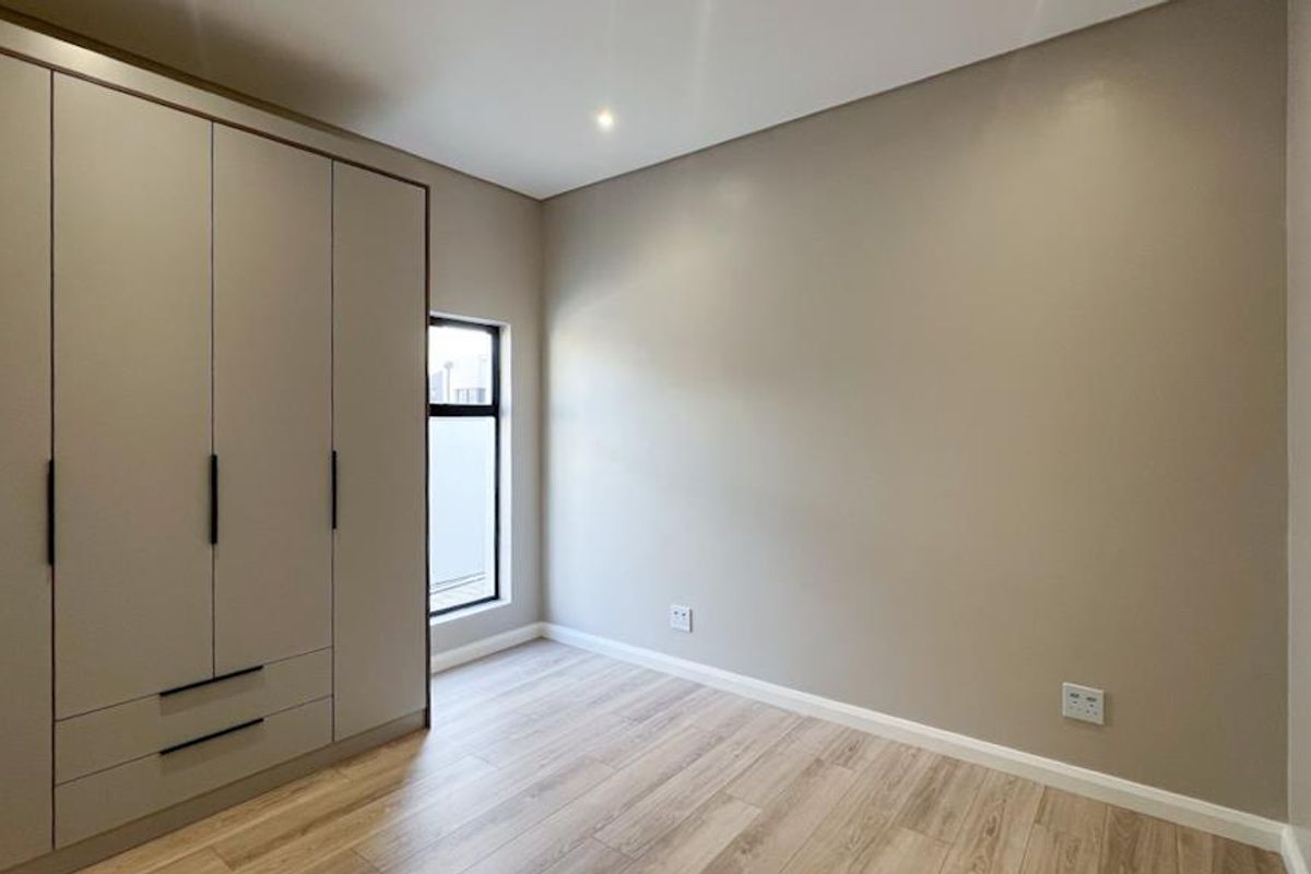 A clean, modern bedroom featuring light wood-look flooring, neutral wall tones, and a large built-in wardrobe with contemporary hardware.