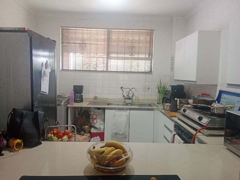 A functional kitchen featuring built-in cabinetry, a double basin sink, tiled splashback, and a gas hob, offering potential for modernization.