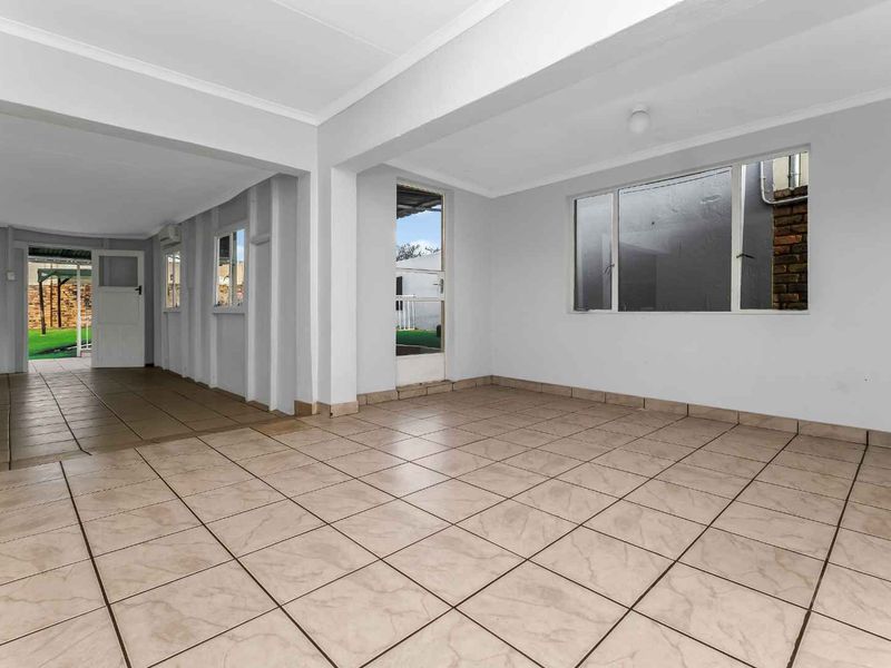 A spacious, empty living area featuring neutral tiled flooring, clean white walls, and large windows providing natural light and access to the outdoor space.