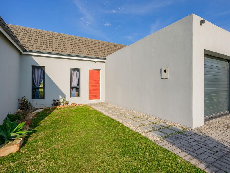 Modern front facade featuring a clean rendered finish, a vibrant red entrance door, a paved driveway, and a well-maintained lawn area.