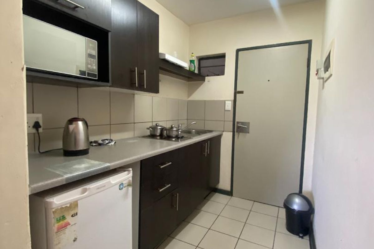 Compact galley-style kitchen featuring dark wood cabinetry, tiled backsplash, integrated sink, and tiled flooring.