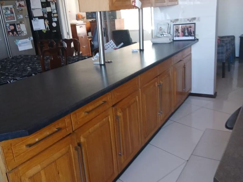 A kitchen featuring wooden cabinetry, a dark laminate breakfast bar, and tiled flooring, offering a functional layout with ample storage space.