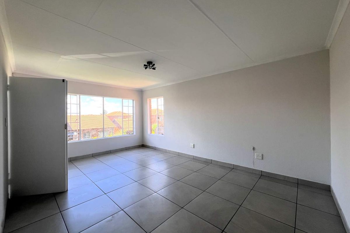 A bright, empty bedroom featuring large windows, tiled flooring, and neutral walls, offering a clean and versatile space ready for personalization.