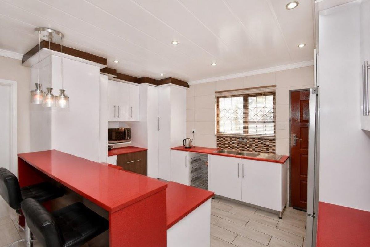 Modern kitchen featuring white cabinetry, vibrant red countertops, a breakfast bar, double sink, and recessed ceiling lighting.