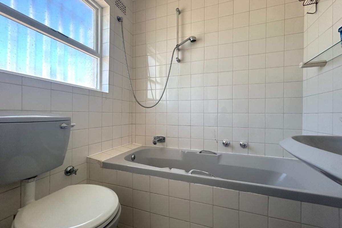 A dated bathroom featuring a grey bathtub, matching toilet, and white wall tiling with a frosted glass window.