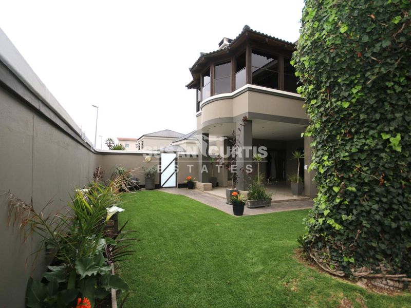 Rear view of the property featuring a well-maintained lawn, a covered patio area, and an upper-level balcony.