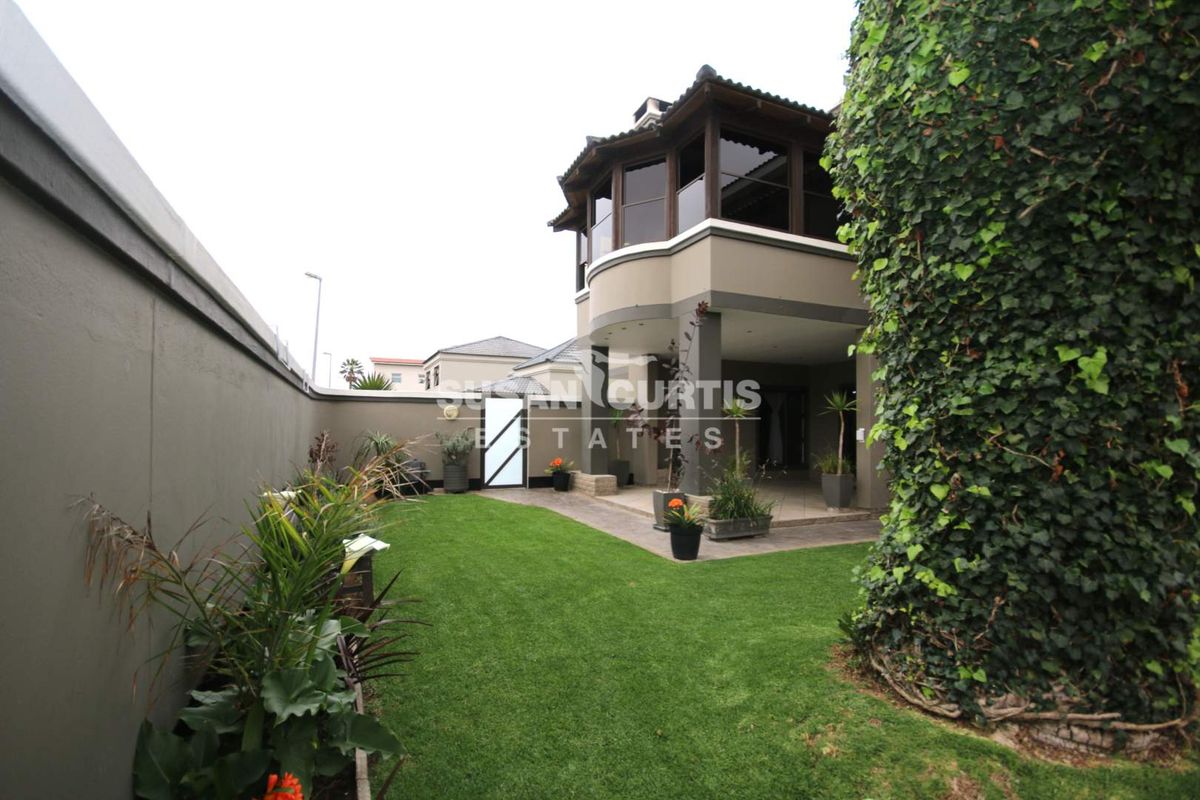 Rear view of the property featuring a well-maintained lawn, a covered patio area, and an upper-level balcony.
