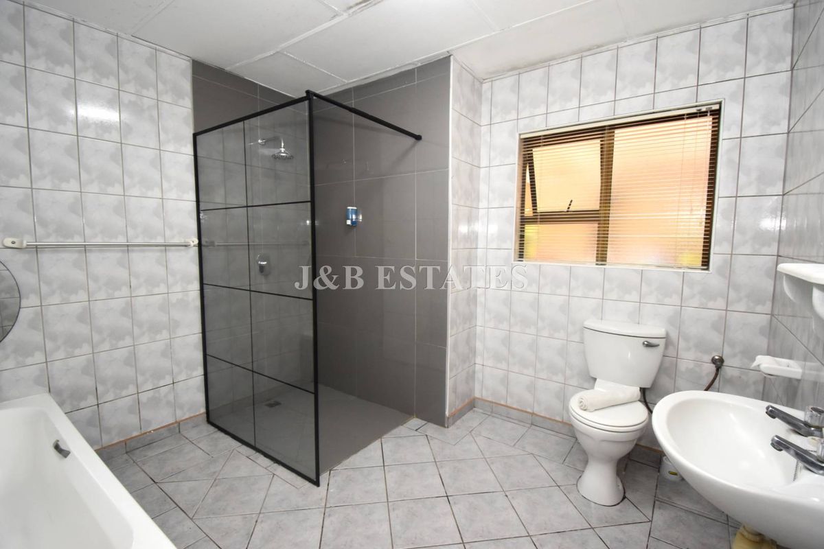 A functional bathroom featuring a walk-in shower with a black frame, a bathtub, a toilet, and a pedestal basin with tiled walls and flooring.