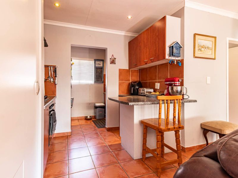 A functional kitchen featuring tiled flooring, built-in cabinetry, a breakfast bar, and a tiled backsplash, with an adjacent scullery or utility area.