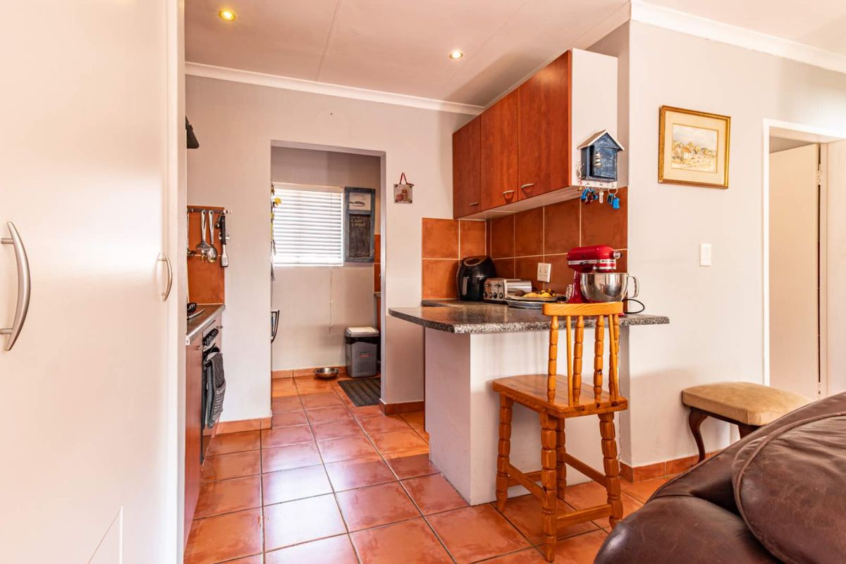A functional kitchen featuring tiled flooring, built-in cabinetry, a breakfast bar, and a tiled backsplash, with an adjacent scullery or utility area.