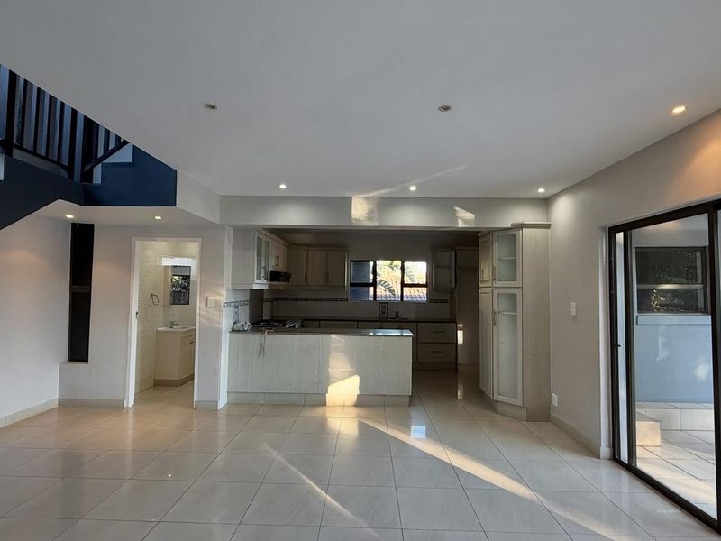 Spacious open-plan living area featuring tiled floors, a modern kitchen with built-in cabinetry, and direct access to an outdoor patio through sliding glass doors.