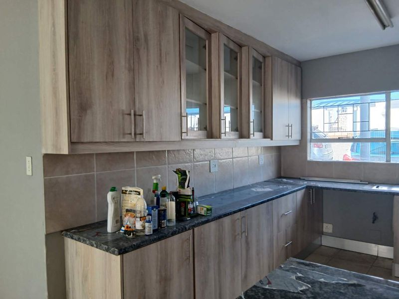 A functional kitchen featuring light wood-grain laminate cabinetry, dark granite countertops, and a tiled backsplash, offering ample storage and workspace.