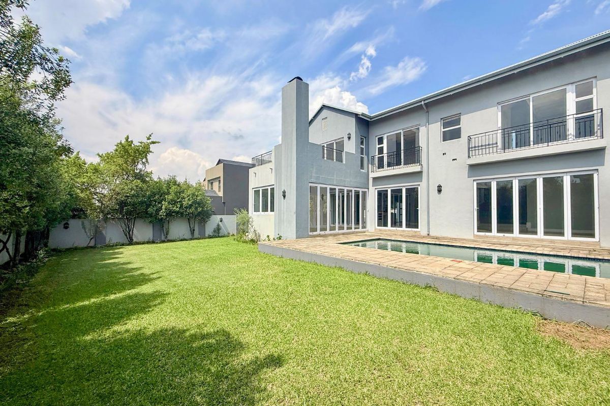 Rear view of a two-story house featuring a swimming pool, paved deck, large sliding glass doors, and upper-level balconies overlooking a landscaped garden.