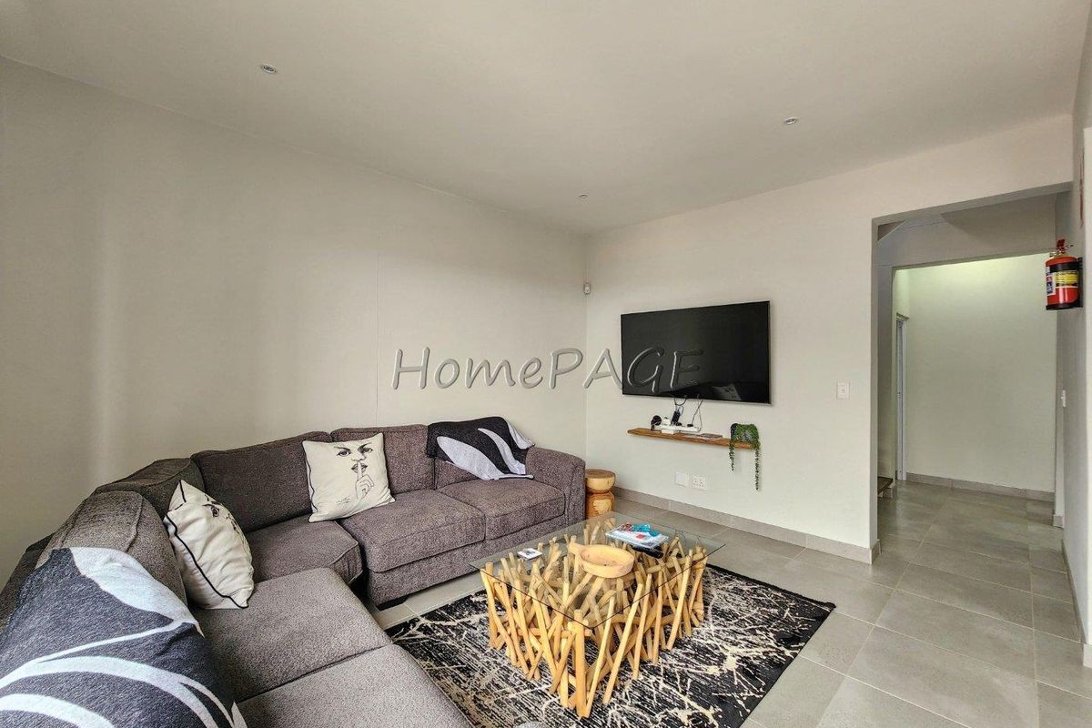 A bright and neutral living room featuring tiled flooring, recessed ceiling lighting, and a wall-mounted television setup.