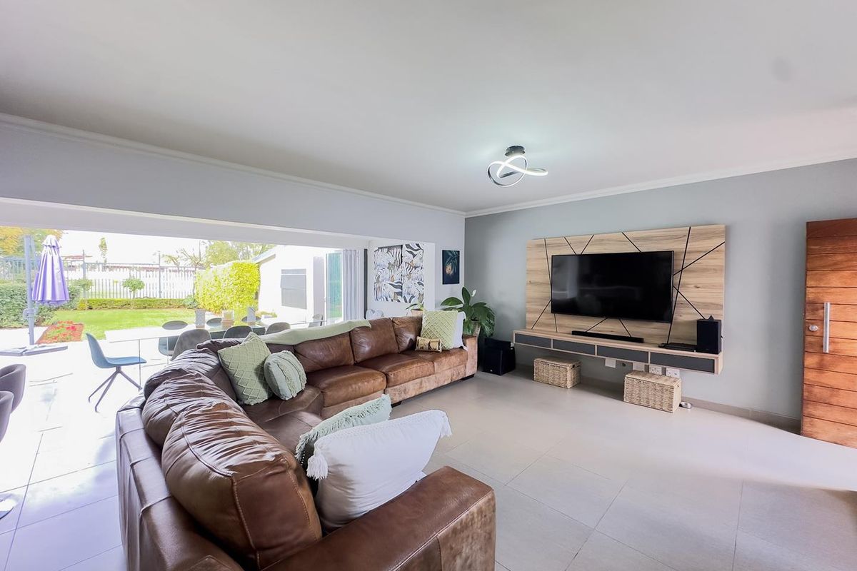 Spacious living room featuring large sliding doors opening to the garden, tiled flooring, and a modern built-in media wall unit.