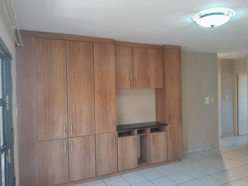 A bright living area featuring extensive built-in wooden cabinetry with integrated shelving and tiled flooring throughout.