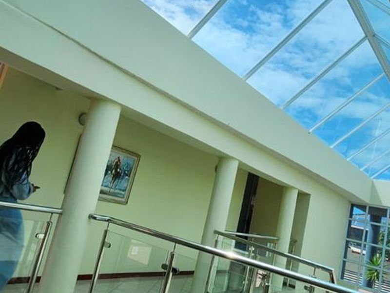 Spacious upper-level hallway featuring a large glass skylight, modern glass balustrade with stainless steel handrails, and tiled flooring.
