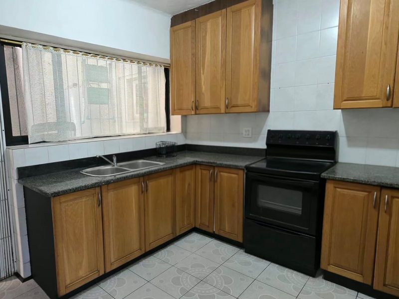A functional kitchen featuring wooden cabinetry, granite countertops, a double basin sink, and a freestanding oven with tiled backsplash and flooring.