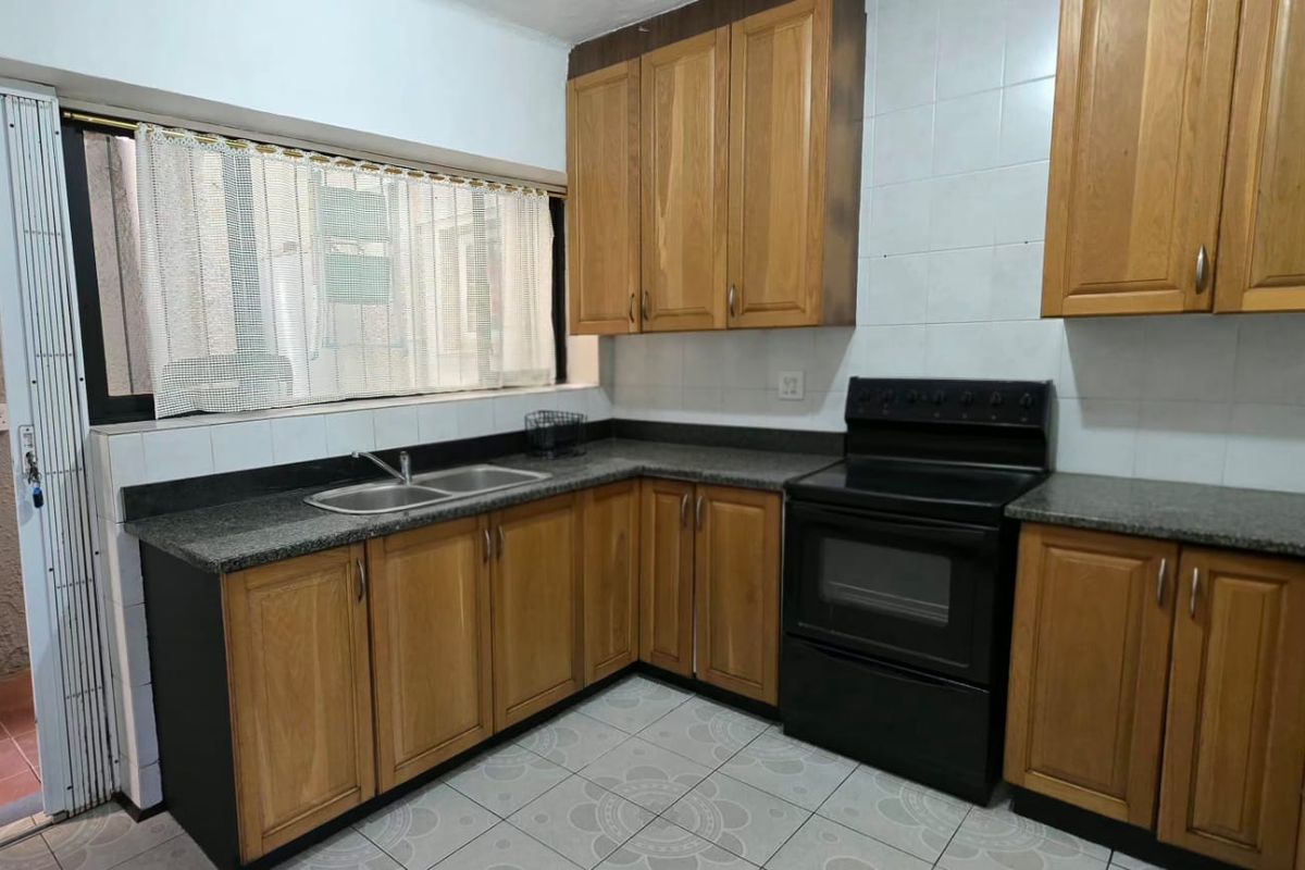 A functional kitchen featuring wooden cabinetry, granite countertops, a double basin sink, and a freestanding oven with tiled backsplash and flooring.
