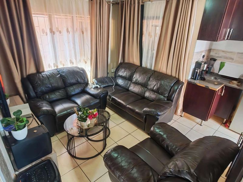 An open-plan living area featuring tiled flooring and an integrated kitchen space with built-in cabinetry and sink.