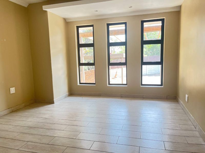 A bright, empty living room featuring modern tiled flooring, recessed downlights, and large aluminium-framed windows allowing for ample natural light.