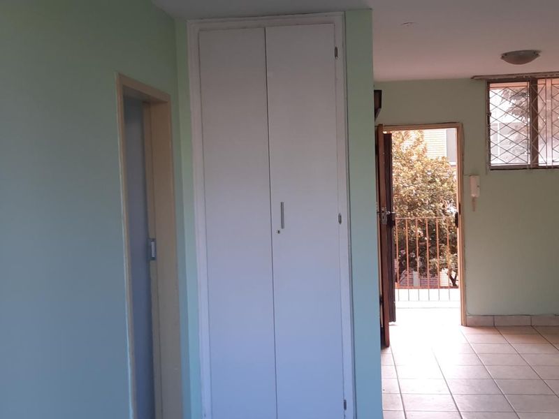 An empty bedroom featuring built-in cupboards, tiled flooring, and access to a small balcony with security gate and window bars.