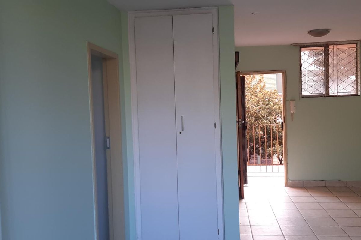 An empty bedroom featuring built-in cupboards, tiled flooring, and access to a small balcony with security gate and window bars.